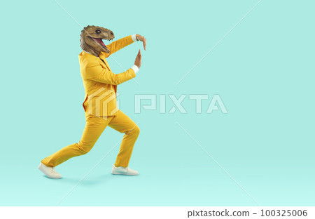 Cheerful and eccentric man in rubber dinosaur mask shows funny dance moves near copy space. 100325006