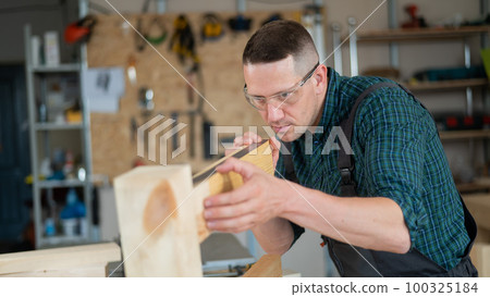Carpenter measures wooden planks in the workshop. 100325184