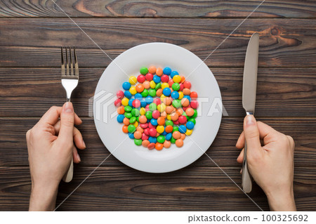 the girl holds cutlery in her hands and eats sweets in a plate. Health and obesity concept, top view on colored background the girl holds cutlery in her hands and eats sweets in a plate. Health and obesity concept, top view on colored background 100325692