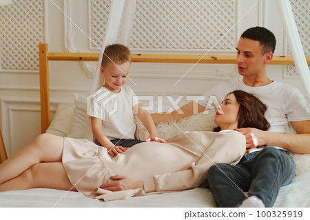 Happy pregnant mom, dad and son play in bed. the concept of family happiness. 100325919