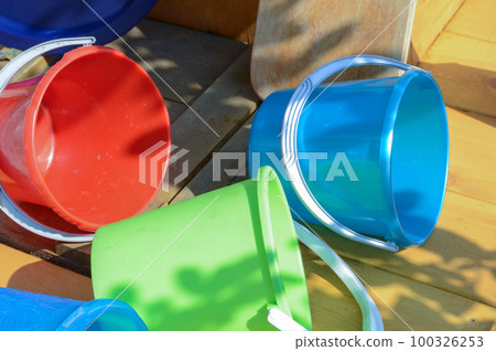Multicolored empty clean plastic tableware on a wooden background, outdoors, on a sunny summer day Multicolored empty clean plastic tableware on a wooden background, outdoors, on a sunny summer day 100326253