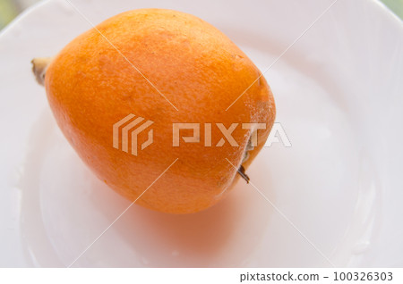 One ripe medlar fruit on a white plate, close-up One ripe medlar fruit on a white plate, close-up 100326303