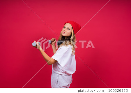 Kid girl doing fitness exercises with dumbbells on red background 100326353