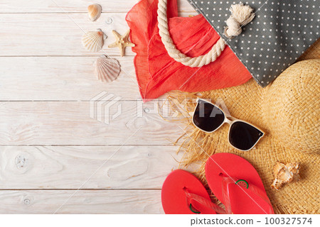 Straw hat sunglasses flip flops and beach bag with scarf on white wooden background 100327574