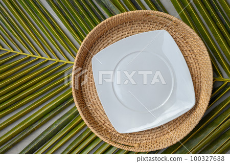 Empty square white plate in authentic wicker tray on green palm leaf. Empty square white plate in authentic wicker tray on green palm leaf. 100327688