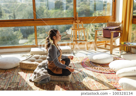 Young woman artist sitting on floor doing yoga exercise at art studio.Mindful activity and art therapy concept Young woman artist sitting on floor doing yoga exercise at art studio.Mindful activity and art therapy concept 100328134