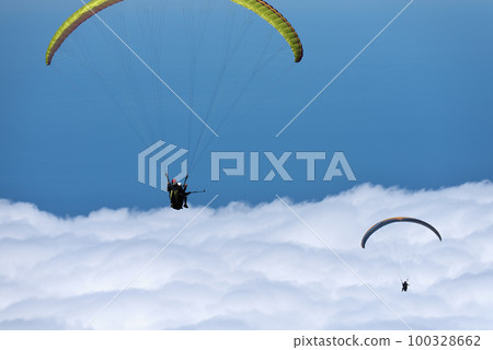 Flight above the clouds, paragliders are flying on a paraglider in the sky. Tandem flight above the clouds Flight above the clouds, paragliders are flying on a paraglider in the sky. Tandem flight above the clouds 100328662