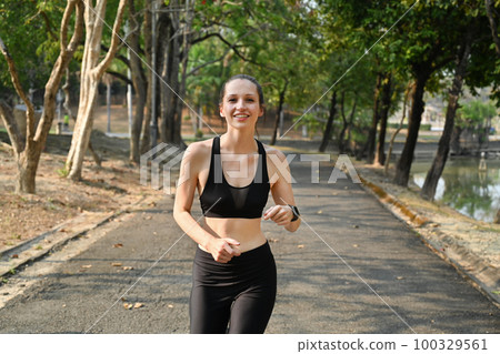 Delighted caucasian female athlete in sportswear jogging in public park, fitness and sport concept 100329561