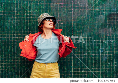 Hipster young woman in bright clothes, sun glasses and bucket hat posing on the green tile wall background. Urban city street fashion. Fashion blogger. Selective focus. Copy space, Hipster young woman in bright clothes, sun glasses and bucket hat posing on the green tile wall background. Urban city street fashion. Fashion blogger. Selective focus. Copy space, 100329764