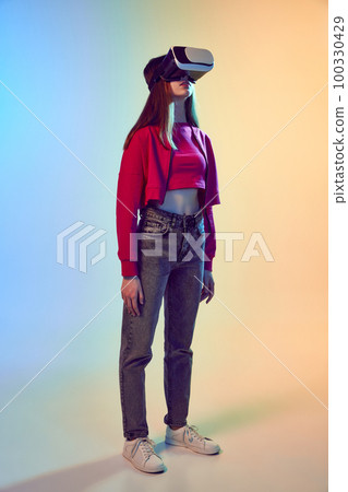 One teen girl wearing VR headset glasses over gradient blue-yellow background. Youth and virtual lifestyle of future. Concept of games, digitalization and technology 100330429