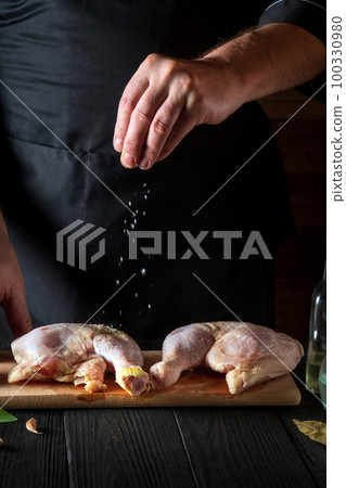 The cook adds salt to the chicken legs. Preparation for grilling with chicken leg in the kitchen of a restaurant or cafe on table with vegetables and spices The cook adds salt to the chicken legs. Preparation for grilling with chicken leg in the kitchen of a restaurant or cafe on table with vegetables and spices 100330980