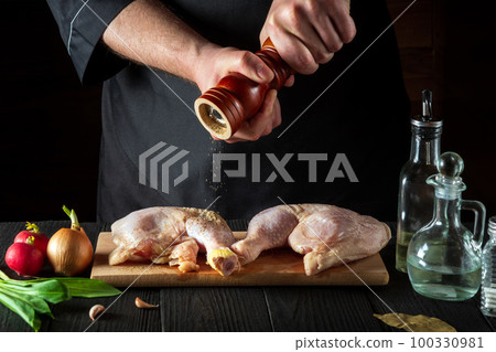 The chef adds pepper to the chicken legs. Grill blank with chicken leg in the kitchen of a restaurant or cafe on table with vegetables and spices The chef adds pepper to the chicken legs. Grill blank with chicken leg in the kitchen of a restaurant or cafe on table with vegetables and spices 100330981