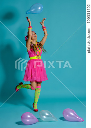 Lovely girl with a multi-colored braids hairstyle and bright make-up, posing in studio with air balloons against a blue background. 100331302