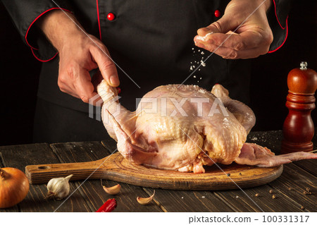 Cooking chicken in the kitchen with the hands of a cook. Before baking, the chef adds salt to raw chicken. Asian cuisine Cooking chicken in the kitchen with the hands of a cook. Before baking, the chef adds salt to raw chicken. Asian cuisine 100331317