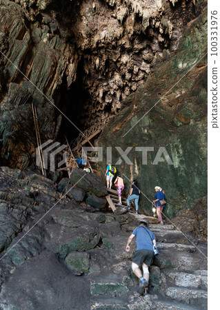 Local tour guide with traditional lantern guiding tourists through the tall and dark chambers of Tham Nam Lod caves Local tour guide with traditional lantern guiding tourists through the tall and dark chambers of Tham Nam Lod caves 100331976