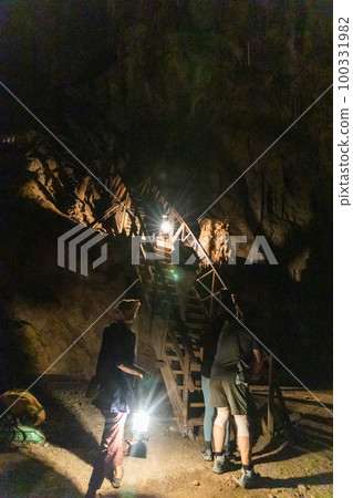 Local tour guide with traditional lantern guiding tourists through the dark chambers of Tham Nam Lod caves 100331982