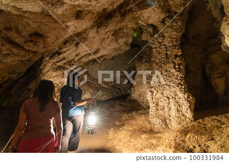 Local tour guide with traditional lantern guiding tourists through the dark chambers of Tham Nam Lod caves 100331984
