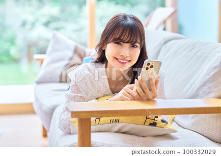 Young woman looking at her smartphone in her room Young woman looking at her smartphone in her room 100332029