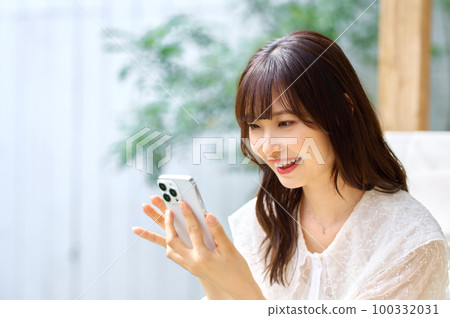 一位年輕女子在房間裡看著她的智慧型手機 100332031