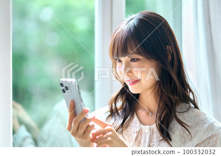 一位年輕女子在房間裡看著她的智慧型手機 100332032