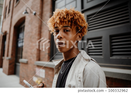 Portrait of the young african american man with serious expression leaning on the wall at street 100332962