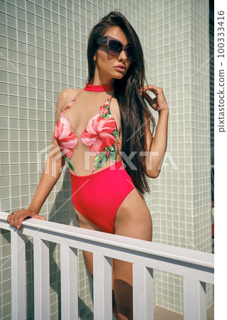 Portrait of a woman having rest in a recreation center or hotel with a swimming pool. Dressed in a colorful swimsuit and sunglasses. Portrait of a woman having rest in a recreation center or hotel with a swimming pool. Dressed in a colorful swimsuit and sunglasses. 100333416