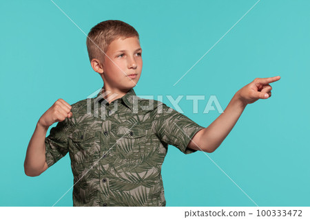 Close-up portrait of a blonde teenage boy in a green shirt with palm print posing against a blue studio background. Concept of sincere emotions. Close-up portrait of a blonde teenage boy in a green shirt with palm print posing against a blue studio background. Concept of sincere emotions. 100333472