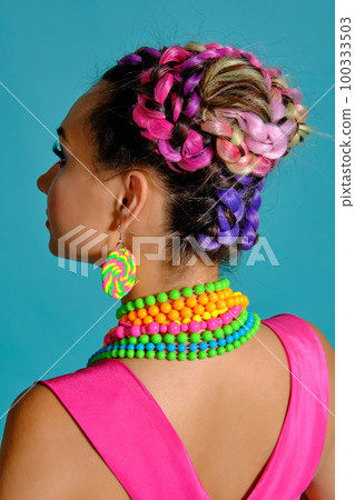 Lovely girl with a multi-colored braids hairstyle and bright make-up, posing in studio against a blue background. Lovely girl with a multi-colored braids hairstyle and bright make-up, posing in studio against a blue background. 100333503