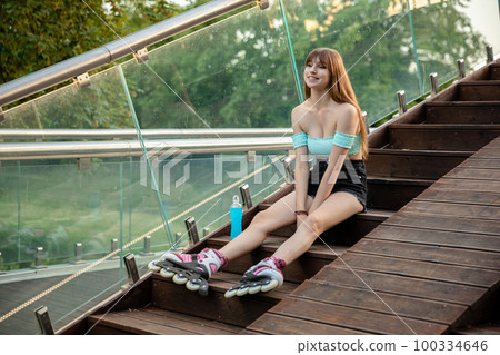 A long-haired girl sits on a wooden staircase and rests after roller-skating. A long-haired girl sits on a wooden staircase and rests after roller-skating. 100334646