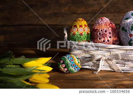 A basket with Easter eggs on a background of boards and tulips lying next to it. A basket with Easter eggs on a background of boards and tulips lying next to it. 100334656