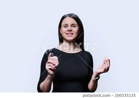 Young woman using bottle of perfume, on white studio background 100335135