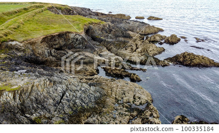 A picturesque stone cape covered with green grass. A rock on the seashore. The rocky coast of the Atlantic Ocean. The coastline. Seaside landscape, rock formation near body of water. 100335184
