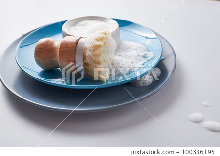 Solid dish washing soap, covered with foam. Zero waste lifestyle. Dishwashing pile of plates with foamy kitchen cleaning sisal bamboo round dish brush. Solid dish washing soap, covered with foam. Zero waste lifestyle. Dishwashing pile of plates with foamy kitchen cleaning sisal bamboo round dish brush. 100336195
