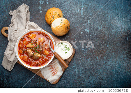 Ukrainian Borscht, red beetroot soup with meat, in white bowl with sour cream, garlic buns Pampushka and salo slices, rustic stone background. Traditional authentic dish of Ukraine, space for text Ukrainian Borscht, red beetroot soup with meat, in white bowl with sour cream, garlic buns Pampushka and salo slices, rustic stone background. Traditional authentic dish of Ukraine, space for text 100336718