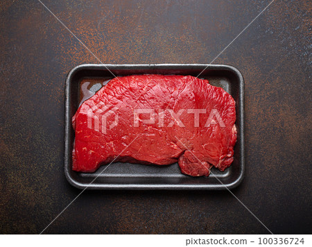 Raw uncooked top round beef steak with blood in black polystyrene tray from supermarket on dark brown rustic stone background from above, defrozing and preparing meat steak Raw uncooked top round beef steak with blood in black polystyrene tray from supermarket on dark brown rustic stone background from above, defrozing and preparing meat steak 100336724