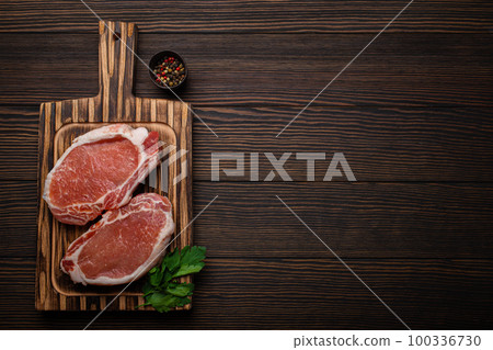 Cut raw meat pork steaks with seasonings on kitchen cutting board, rustic wooden background top view, ready for BBQ. Pork loin chops with space for text Cut raw meat pork steaks with seasonings on kitchen cutting board, rustic wooden background top view, ready for BBQ. Pork loin chops with space for text 100336730