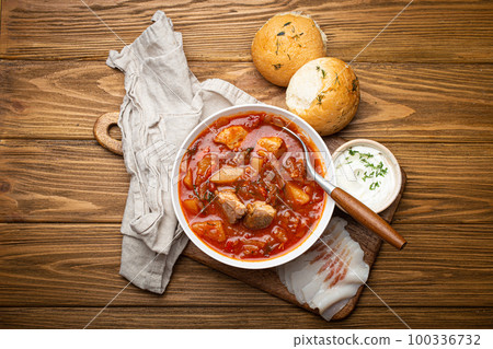 Ukrainian Borscht, red beetroot soup with meat, in white bowl with sour cream, garlic buns Pampushka and salo slices, rustic stone background. Traditional authentic dish of Ukraine 100336732