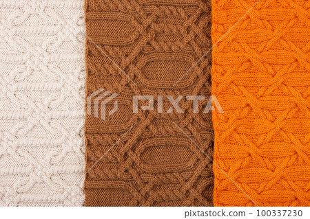 Knitted orange, brown, and beige background. Large knitted fabric with a pattern. Close-up of a knitted blanket. Banner 100337230