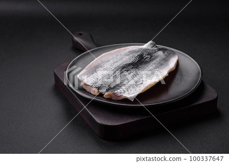 Delicious salted herring fillet in oil on a black ceramic plate Delicious salted herring fillet in oil on a black ceramic plate 100337647