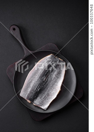 Delicious salted herring fillet in oil on a black ceramic plate Delicious salted herring fillet in oil on a black ceramic plate 100337648