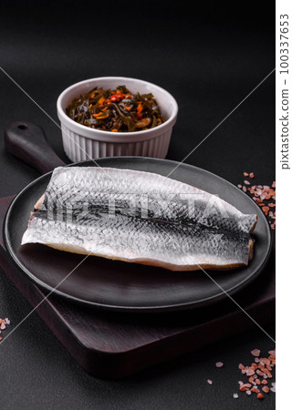 Delicious salted herring fillet in oil on a black ceramic plate 100337653