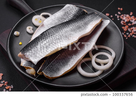 Delicious salted herring fillet in oil on a black ceramic plate Delicious salted herring fillet in oil on a black ceramic plate 100337656