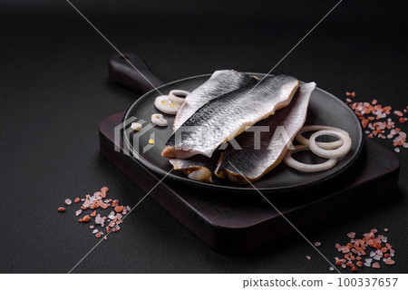 Delicious salted herring fillet in oil on a black ceramic plate Delicious salted herring fillet in oil on a black ceramic plate 100337657