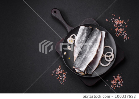 Delicious salted herring fillet in oil on a black ceramic plate Delicious salted herring fillet in oil on a black ceramic plate 100337658