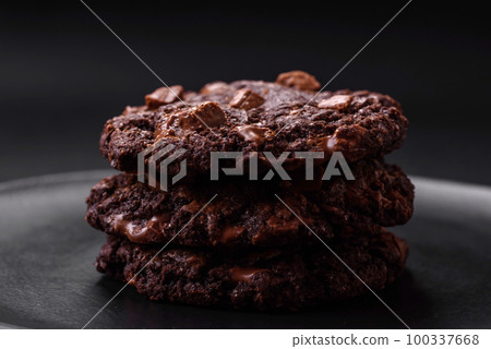 Delicious fresh oatmeal round cookies with chocolate on a black ceramic plate 100337668