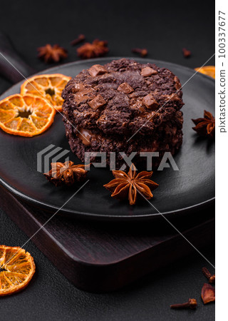 Delicious fresh oatmeal round cookies with chocolate on a black ceramic plate 100337677