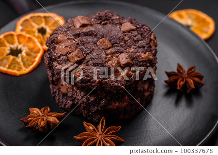 Delicious fresh oatmeal round cookies with chocolate on a black ceramic plate 100337678