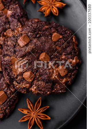 Delicious fresh oatmeal round cookies with chocolate on a black ceramic plate 100337680