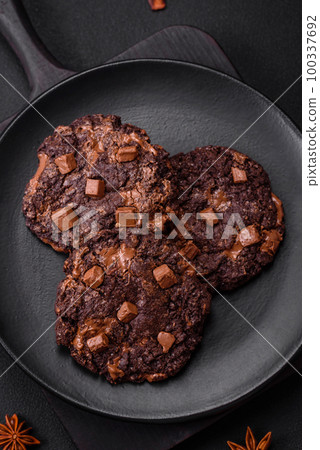 Delicious fresh oatmeal round cookies with chocolate on a black ceramic plate 100337692