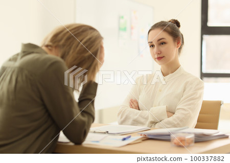 Female manager looks at sad employee while sitting at office desk. 100337882
